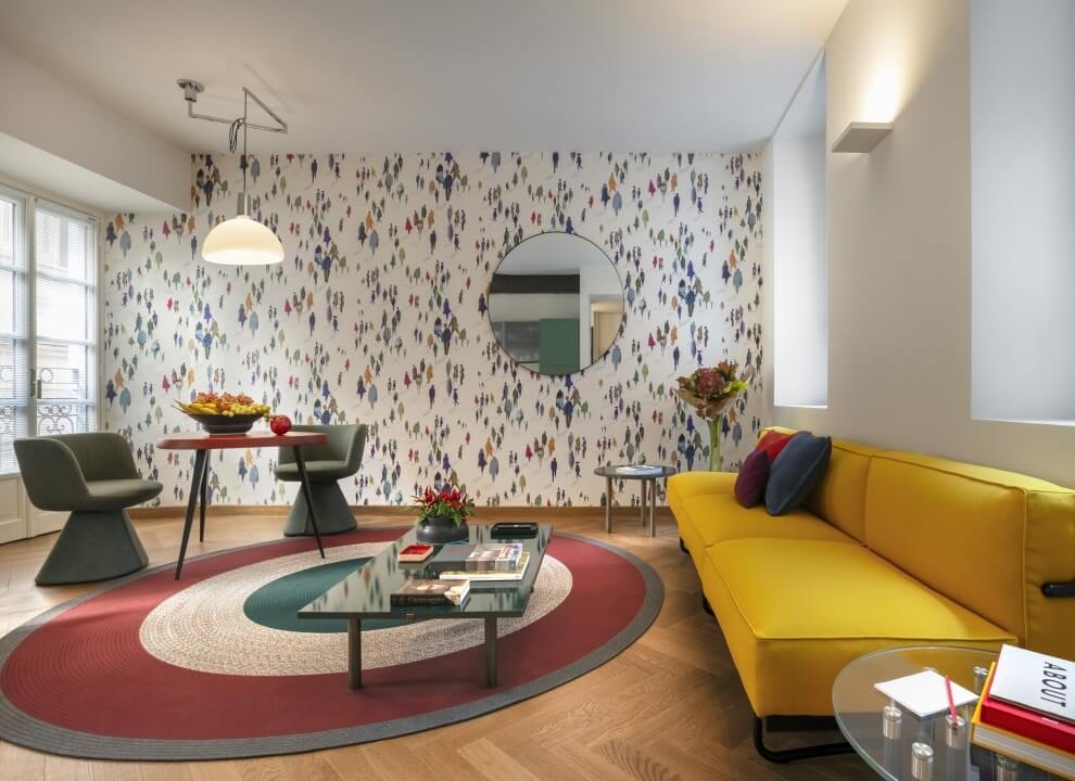 Soggiorno moderno con area pranzo, tavolo rosso, divano giallo, decorazioni e carta da parati astratta colorata.