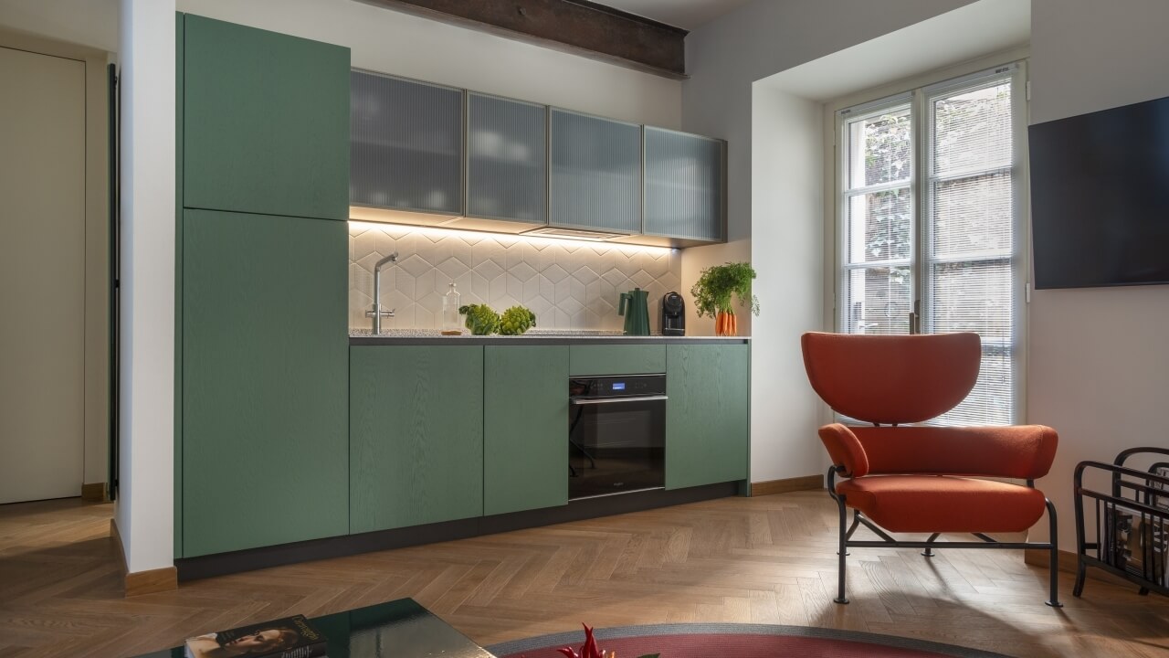 Modern kitchen and living area with green cabinets, white countertop, natural light, and a red rug for color contrast.