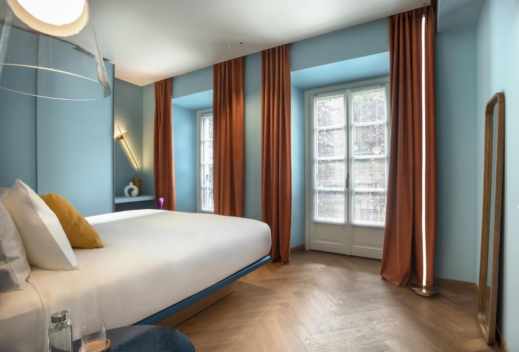 Camera da letto moderna e minimalista con letto bianco, tende arancioni, finestre luminose e decorazioni eleganti.