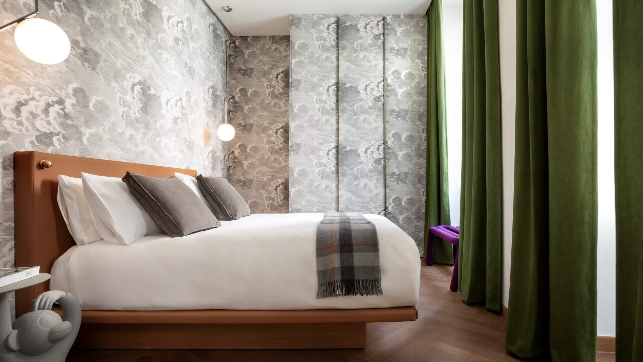 Modern bedroom with a large bed, gray and white wallpaper, purple bench, and natural light from green curtains.