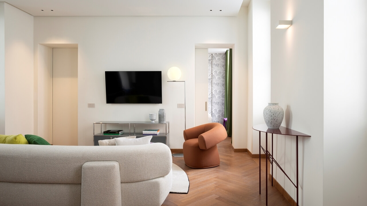 Modern minimalist living room with white couch, orange chair, and a hallway leading to another room.