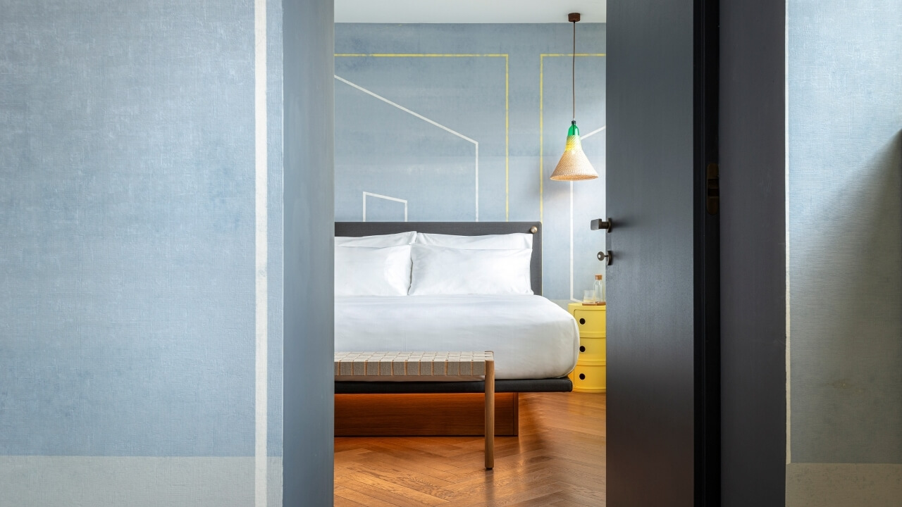 Serene bedroom with light blue walls, a bed with white linens, a yellow nightstand, and a warm hanging lamp.