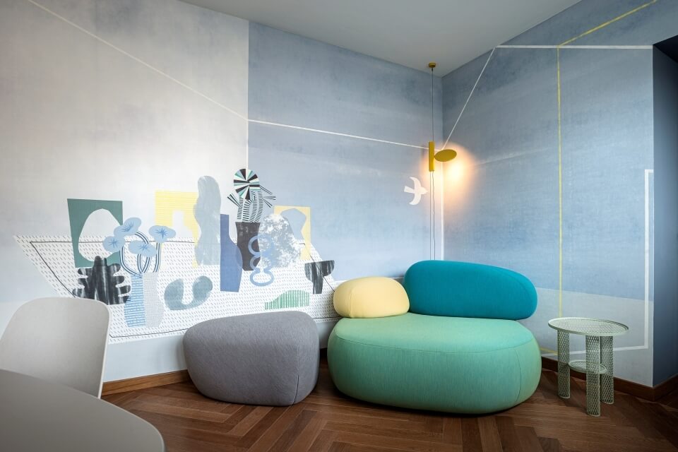 Modern room featuring a colorful couch, white chair, round table, geometric wall art, and wooden floor.