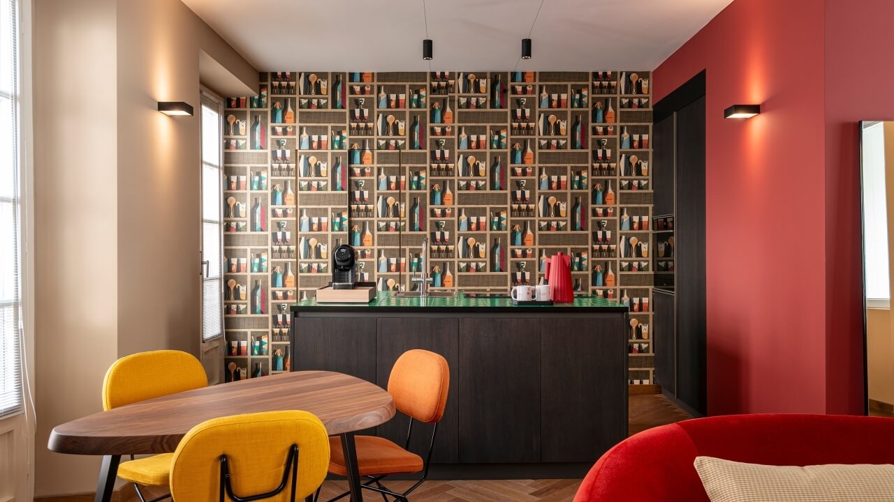 Modern open-concept kitchen with red wall and dark wood cabinet, adjacent to a dining area with a brown wall and oval table.