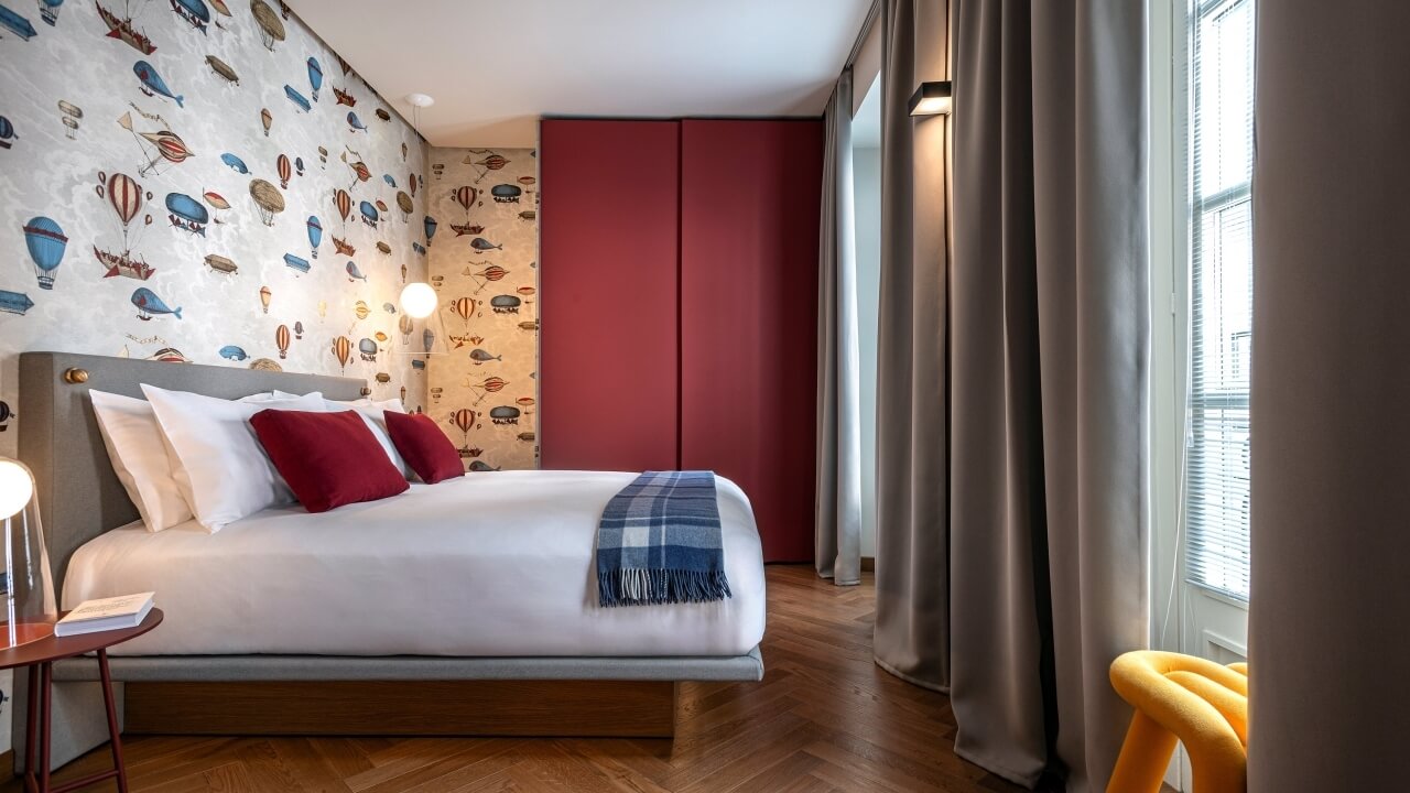 Cozy bedroom with a bed, nightstand, hot air balloon wallpaper, window, yellow chair, and wooden floor.