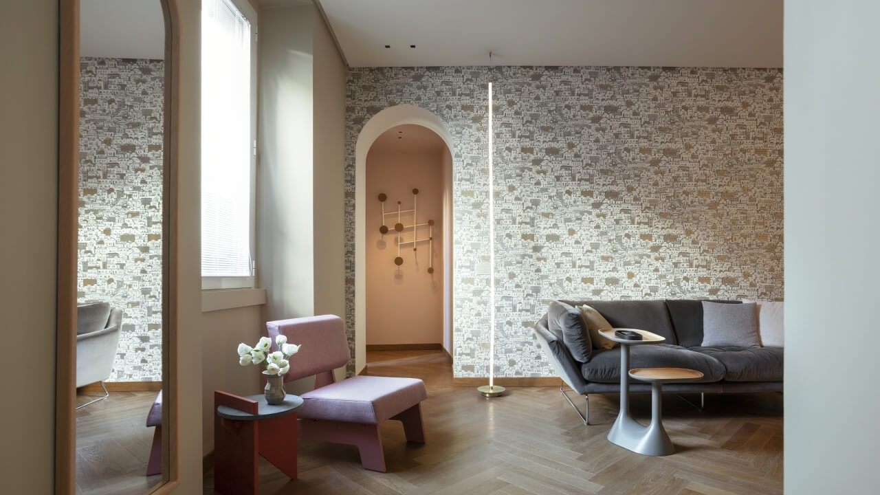 Modern living room with arched entryway, pink hallway, elegant wallpaper, gray couch, pink chair, and warm lighting.