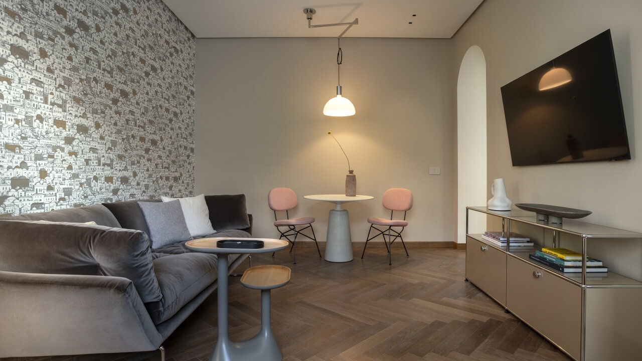 Modern living room with a gray couch, white coffee table, wall-mounted TV, and pendant light, featuring geometric wallpaper.