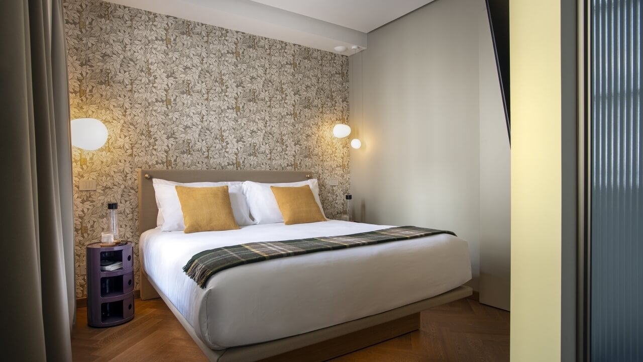 Cozy bedroom with a large bed, white comforter, yellow pillows, green plaid blanket, floral wall, and wooden floor.