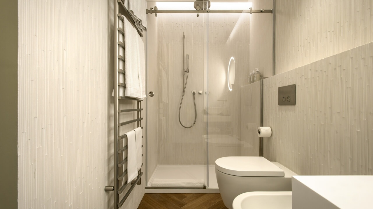 Modern bathroom with glass shower, toilet, sink, towel rack, mirror, and herringbone wood floor, exuding cleanliness.