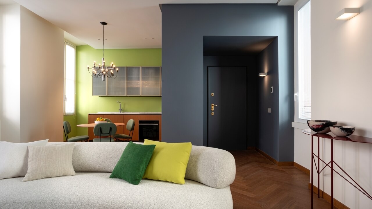 Modern living room with a white couch, colorful pillows, dining area, and kitchen, bathed in natural light.