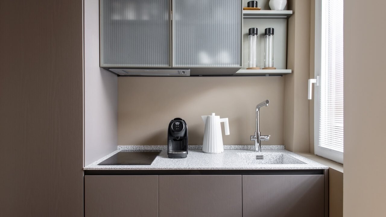 Modern minimalist kitchen with a white countertop, built-in sink, high-end appliances, and natural light from a window.