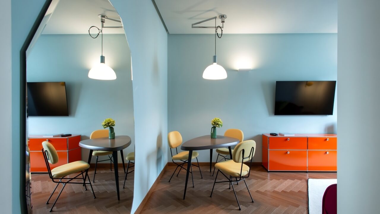 Modern room with two round tables, yellow chairs, orange cabinets, and a TV, featuring a cozy light blue ambiance.