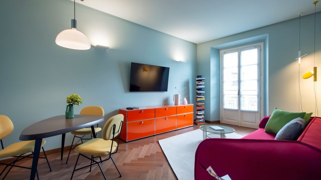 Modern living room with a dining area, featuring a pink sofa, dark oval table, and vibrant decor in natural light.