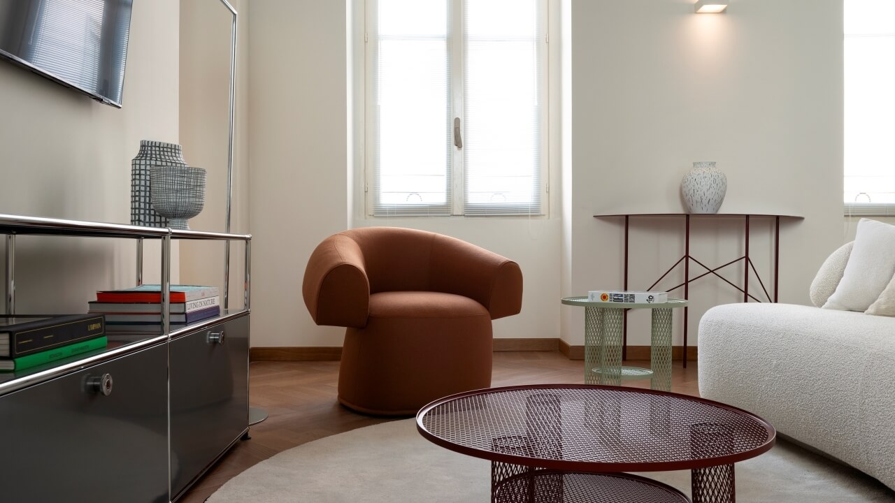 Modern living room with a brown chair, white couch, decorative items, and natural light from three windows.