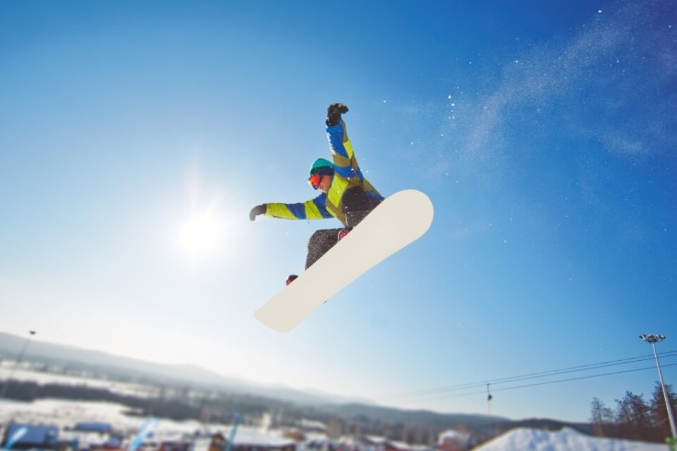Snowboarder mid-air against a bright sky and snowy landscape.   Snowboarder in volo contro un cielo luminoso e paesaggio innevato.