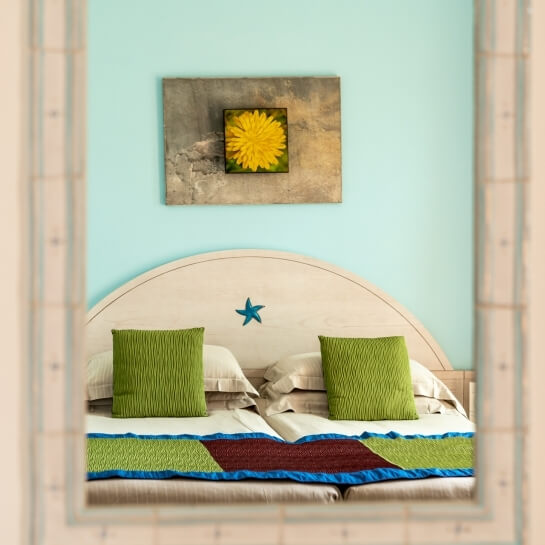 Camera semi-rustica con letto matrimoniale, parete blu, opere d'arte floreale ed ricamata, atmosfera da Airbnb vicino al mare.