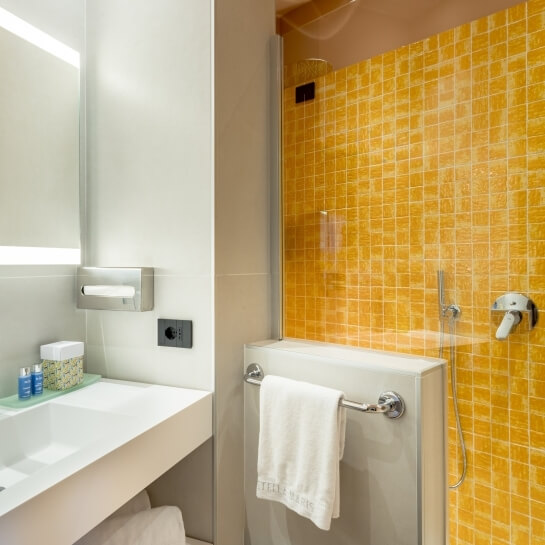 Salle de bain moderne avec lavabo, miroir éclairé et douche carrelée jaune.