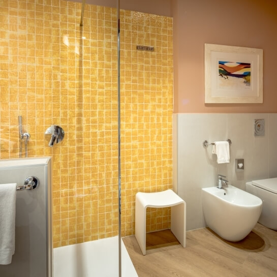 Salle de bain avec douche en verre, carrelage jaune et œuvre d'art.