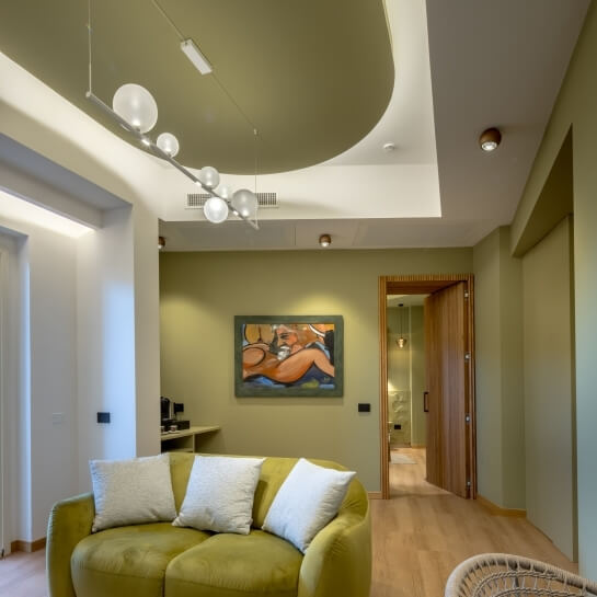 Salon avec canapé vert, coussins blancs, peinture et porte ouverte.