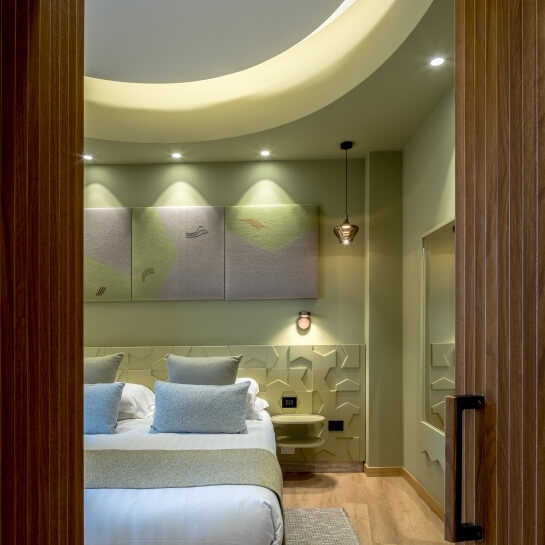 Chambre d'hôtel avec lit blanc, décor vert et art abstrait.