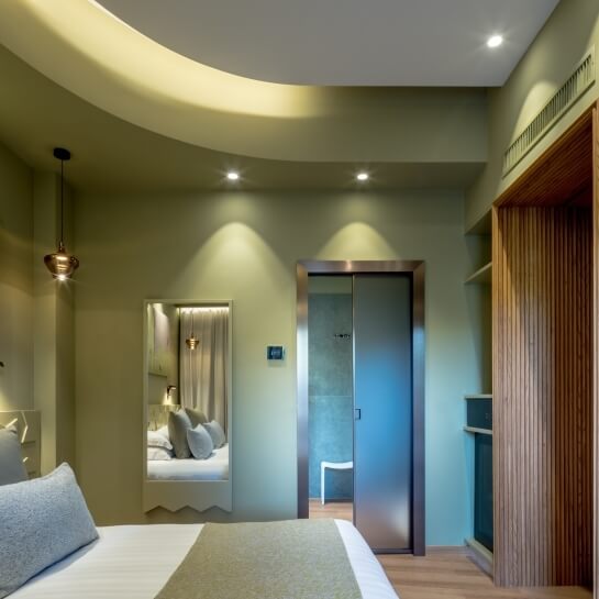 Chambre d'hôtel avec lit blanc et vert, miroir et armoire en bois.