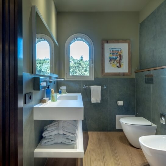 Salle de bain d'hôtel avec lavabo, miroir, fenêtres et peignoirs.