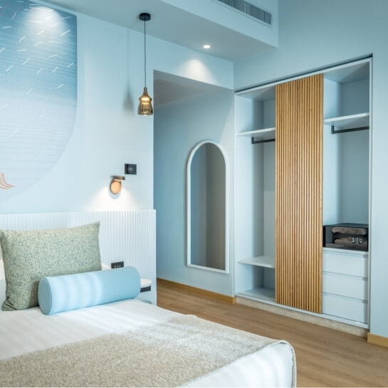 Chambre d'hôtel avec lit, placard, miroir et lampe de sol.