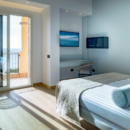 Chambre d'hôtel avec lit, balcon vue océan, bureau et deux télévisions.