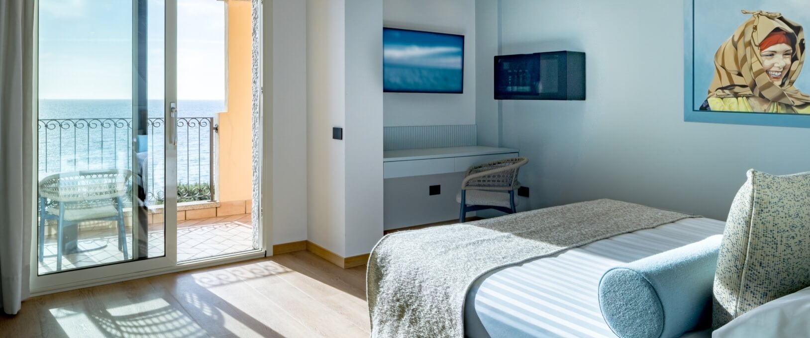 Hotelzimmer mit Meerblick, Balkon, Schreibtisch und zwei Fernsehern.