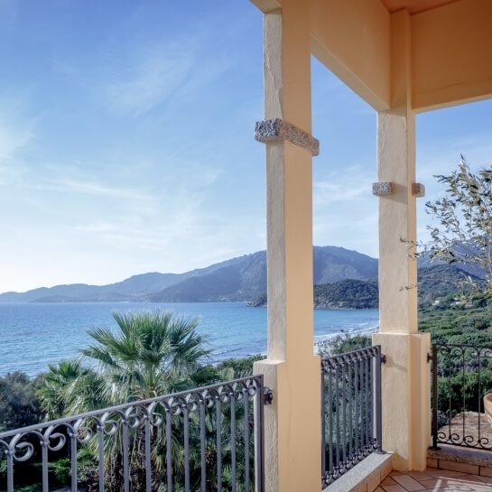 Balcon avec vue sur l'eau, montagnes, palmiers et végétation.