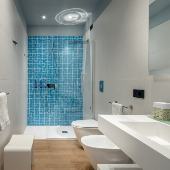 Salle de bain avec douche carrelée bleue, toilettes, bidet et lavabo.