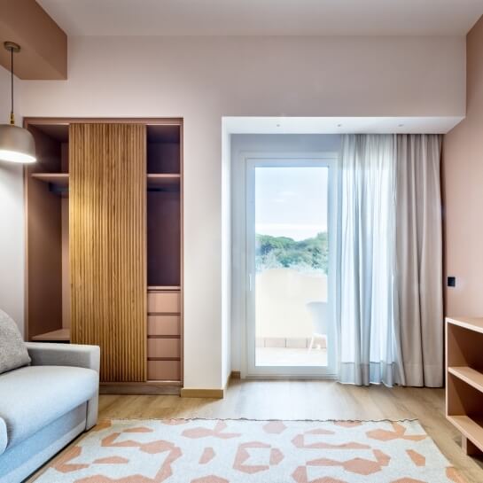 Chambre d'hôtel avec canapé gris, placard en bois et balcon.