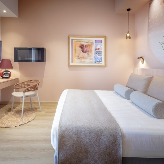 Chambre d'hôtel avec lit, bureau, lampe et décor rose.