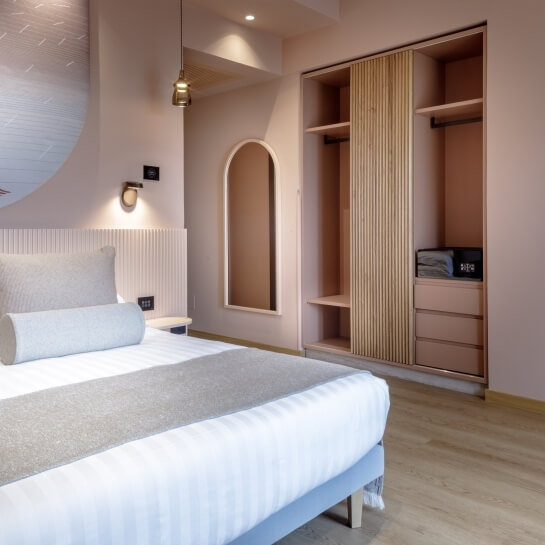 Chambre d'hôtel avec lit, armoire intégrée et miroir arqué.
