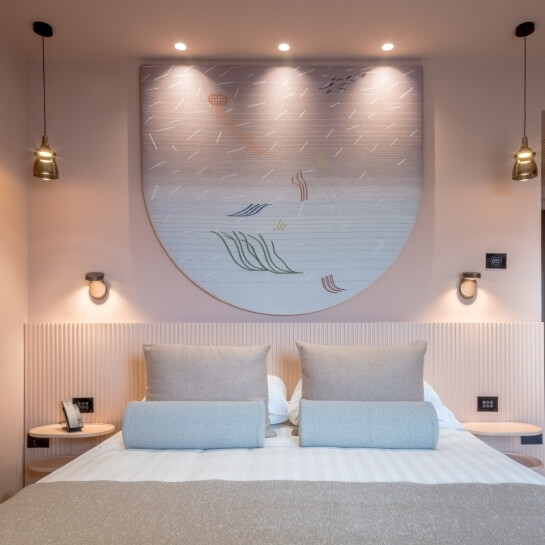 Chambre d'hôtel avec lit, art mural et lampes suspendues.