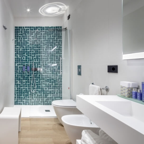 Salle de bain moderne avec lavabo, douche en verre et carrelage mosaïque.