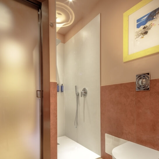 Salle de bain avec douche, toilettes blanches et décoration murale.