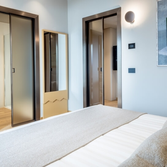 Lit avec linge rayé, miroirs, et deux portes vitrées.