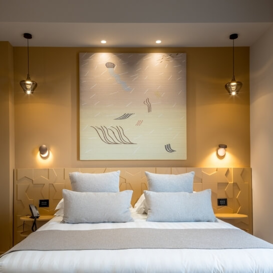 Chambre d'hôtel avec lit, œuvres d'art et éclairage moderne.