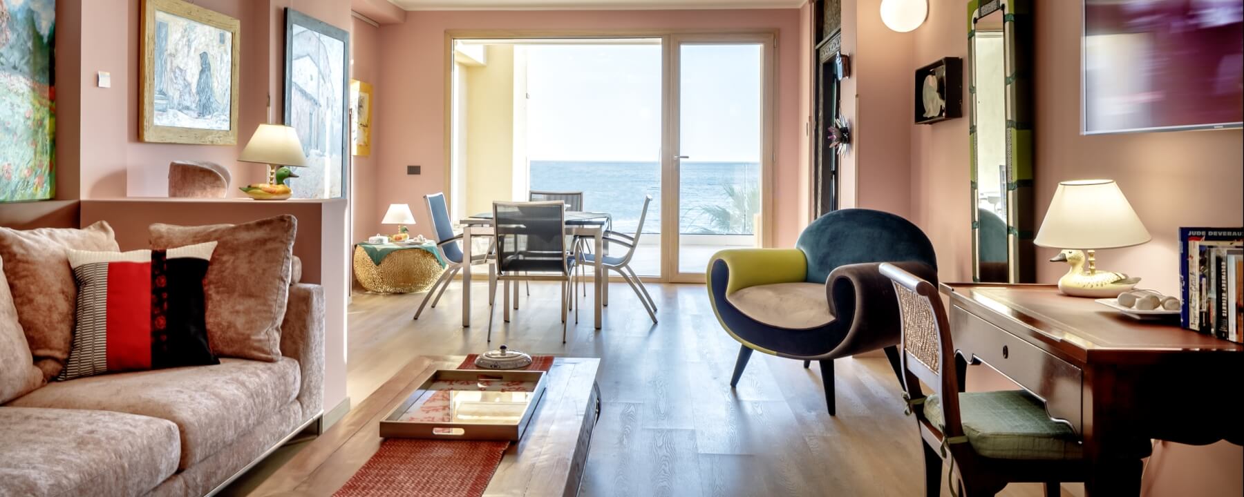 Wohnzimmer mit Meerblick, Couch, Glastisch, Schreibtisch, Stühle und bunten Kissen, schafft eine einladende Atmosphäre.