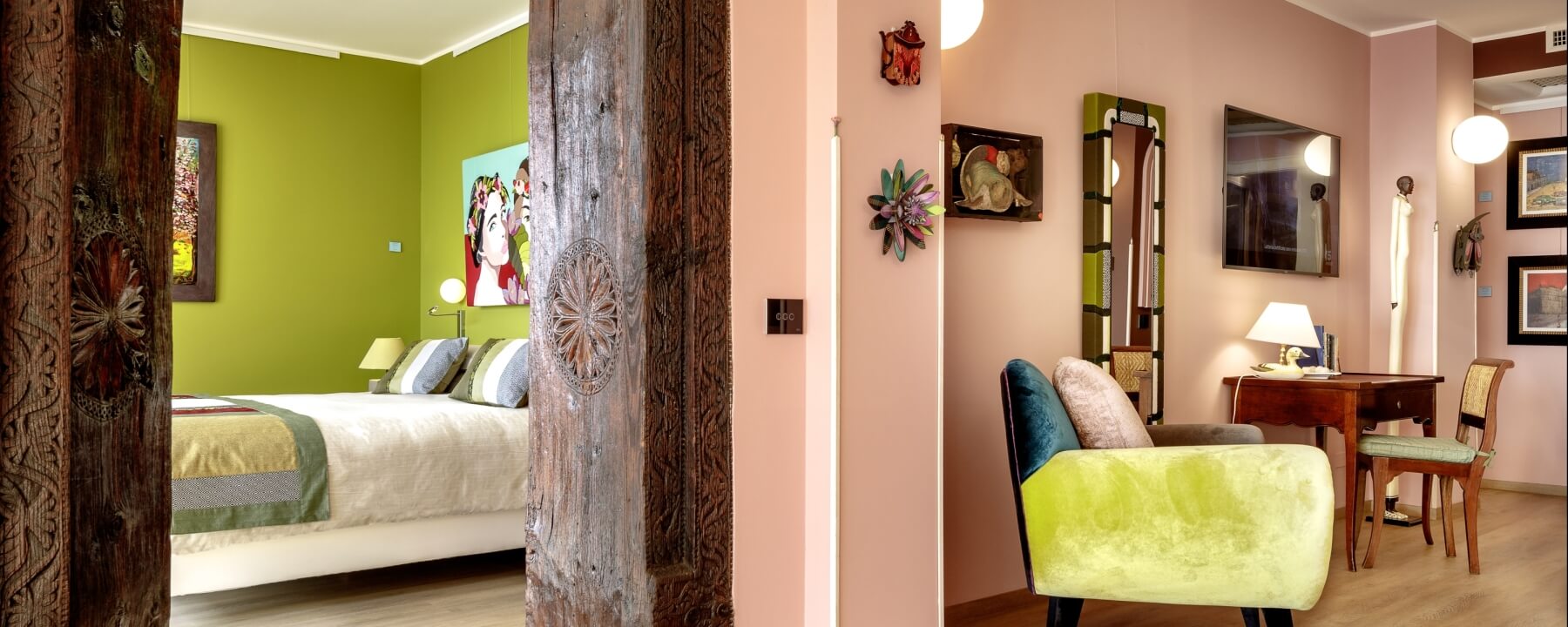 Bild eines Innenraums mit zwei Zimmern: links ein Bett mit grüner Decke, rechts ein Schreibtisch und eine Couch vor einem Spiegel.