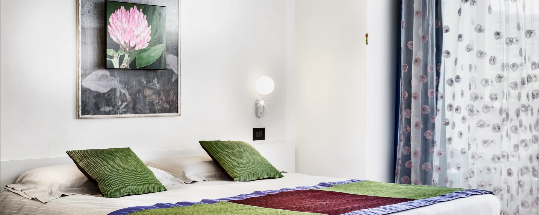 Minimalistisches Schlafzimmer mit einem Bett, weißen Bettwäsche, grünen Kissen, gestreifter Decke und einem Fenster für natürliches Licht.