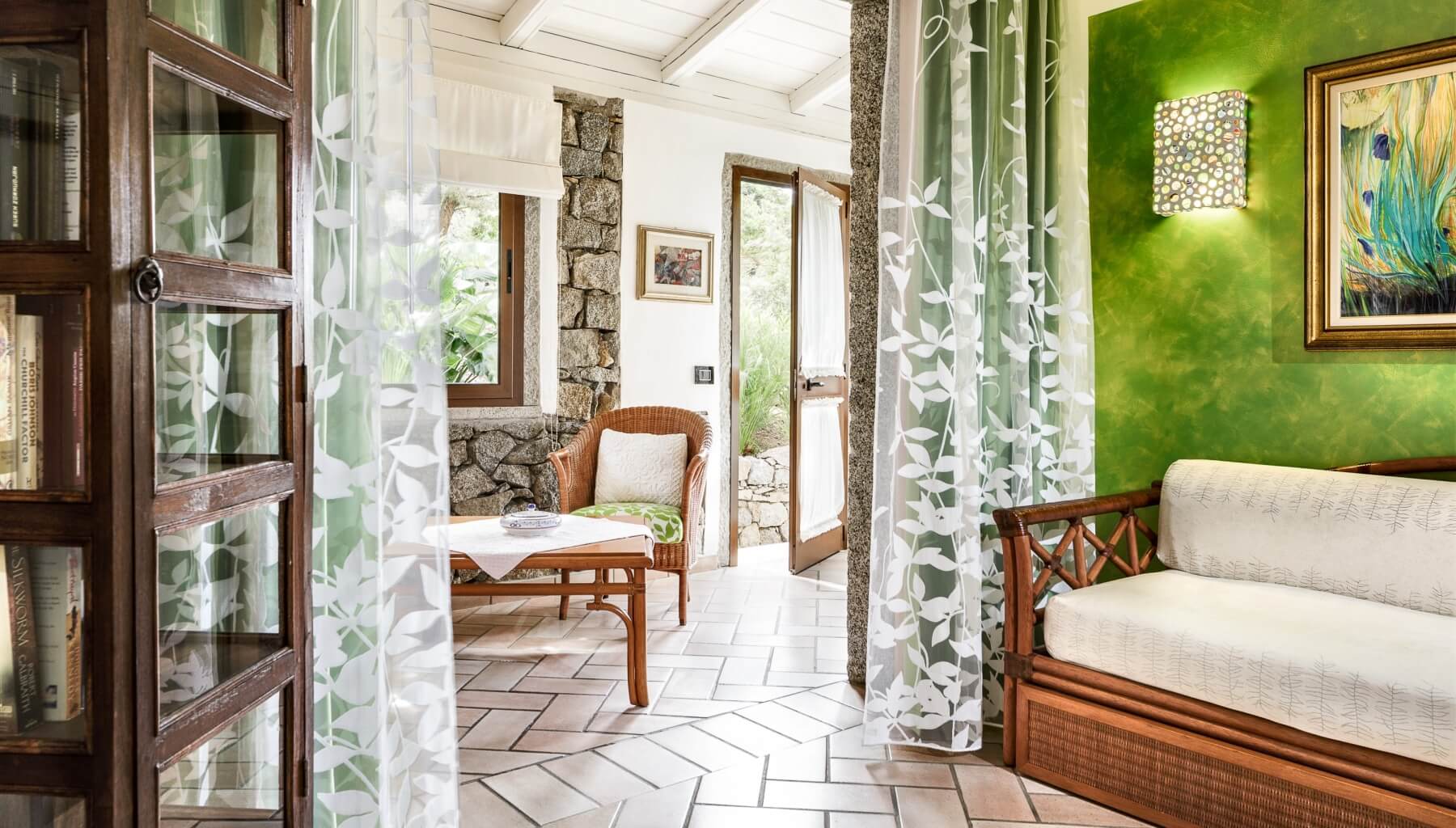 Serene room with white couch, coffee table, sheer leaf-pattern curtains, stone wall, and natural light creating an inviting atmosphere.