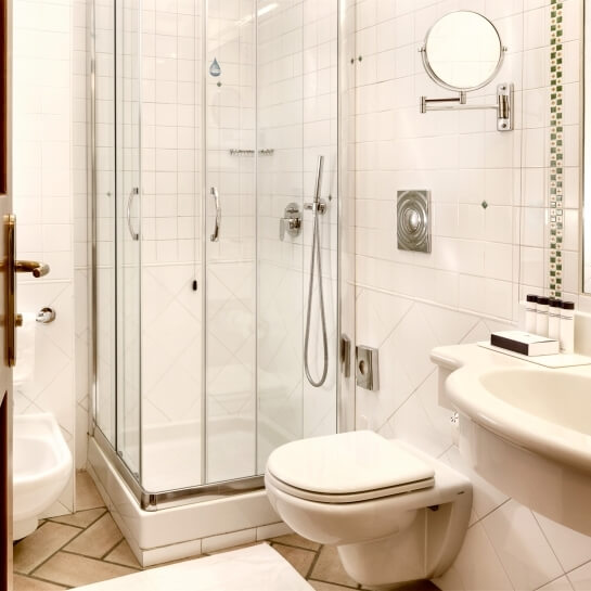 Interno di un bagno moderno con doccia in vetro, sanitari bianchi e piastrelle off-white e grigie.