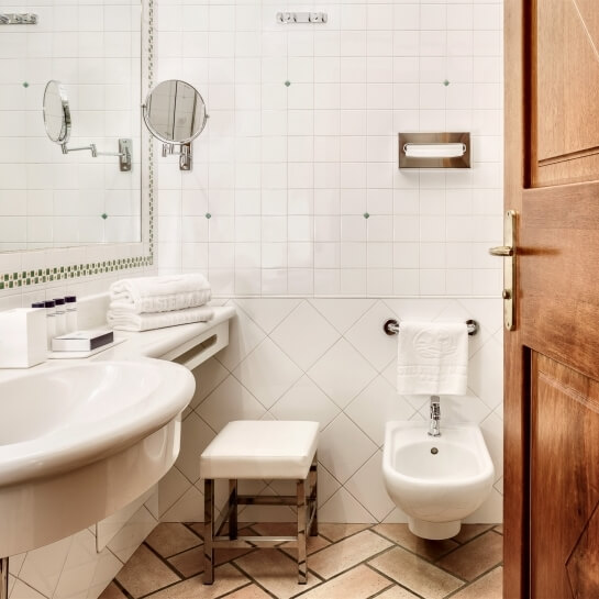 Bagno compatto con lavabo bianco, bidet, specchio, asciugamani e pavimento in piastrelle a spina di pesce.