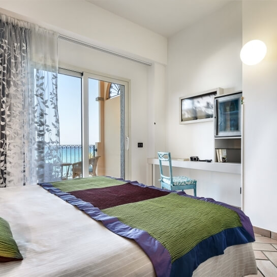 Camera da letto con letto, scrivania e balcone; decorazioni in bianco, blu e verde, luce naturale e atmosfera serena.