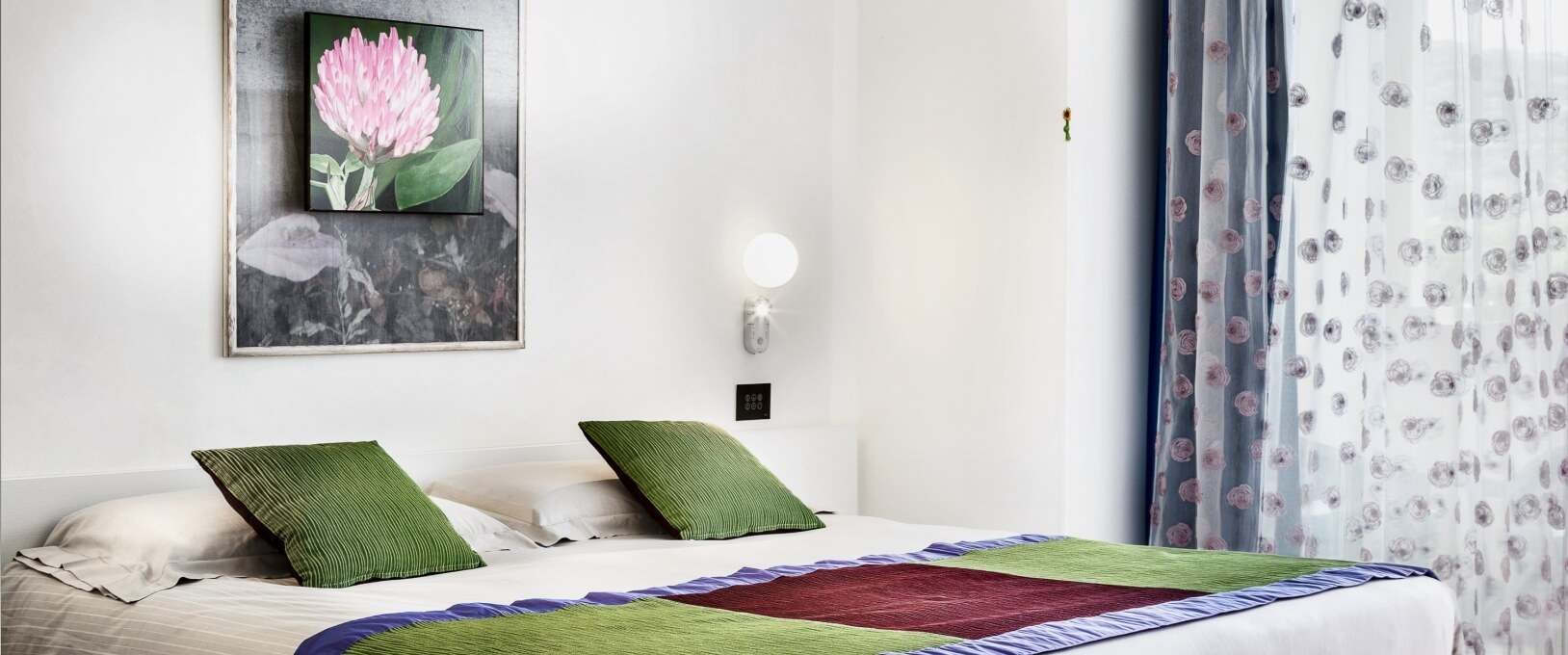 Cozy hotel room with a bed, floral curtains, and framed artwork.