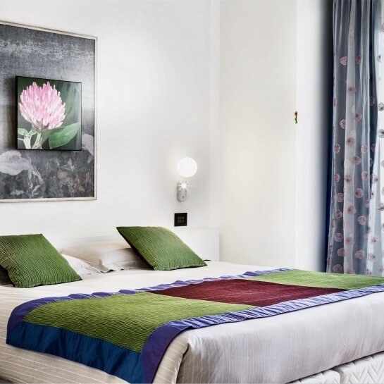 Hotel room bed with white comforter, colorful throw, and framed flower picture.