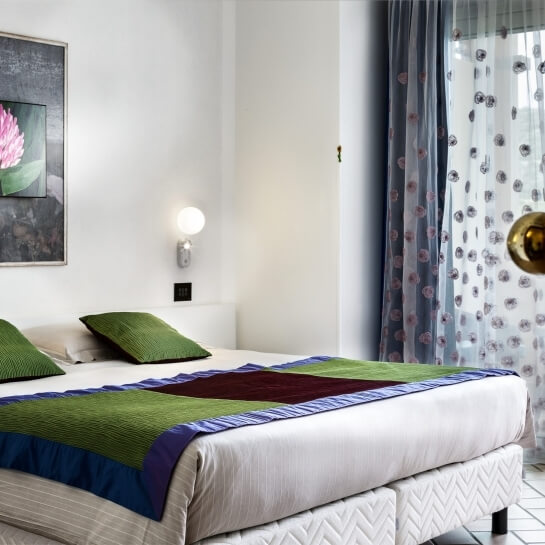 Camera da letto con letto bianco, coperta colorata, decorazioni floreali e luce calda. Atmosfera invitante.