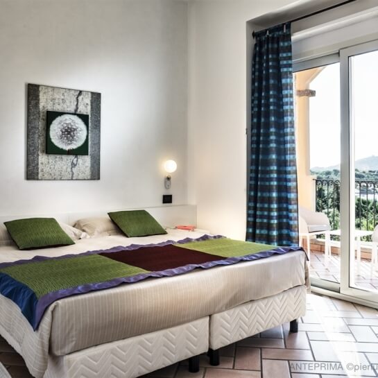 Hotel room with bed, colorful throw, balcony view, and dandelion art.